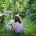 girl and puppy sitting on green grass surrounded with plants during daytime